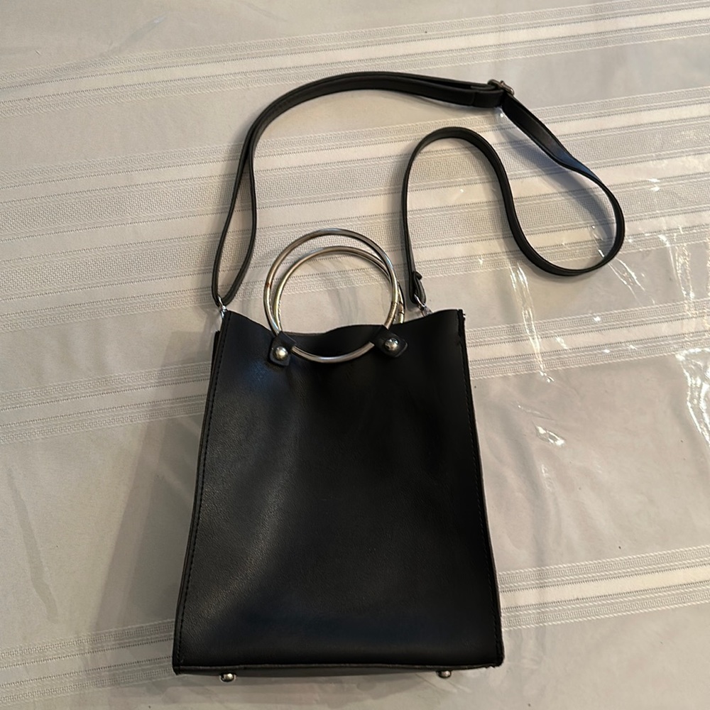 Black pocketbook with silver ring handles and adjustable shoulder strap.